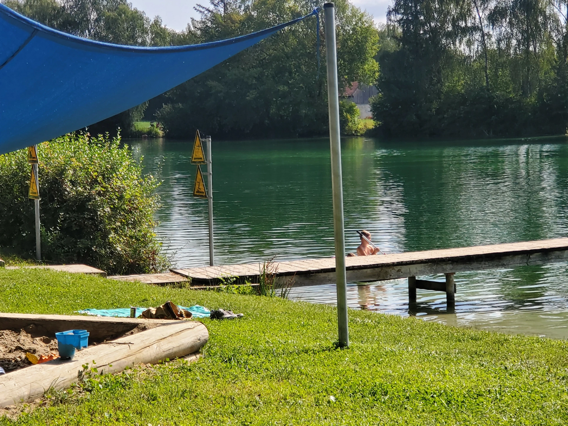 Badesteg und ein Teil des überdachten Sandkastens, im Hintergrund der Lüßer Badeweiher